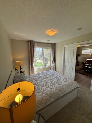 A bedroom with a bed, a lamp, a window, and a door leading to another room.