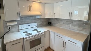 A modern kitchen with white cabinets, a white stove, and a tiled backsplash. - 2 Bed Room, 1 Bath, Living, Kitchen, Office, Bright, Walkout Basement Suite (Calgary)
