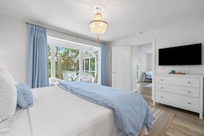 Ein Schlafzimmer mit Bett, Fernseher, Kommode und Blick ins Freie.