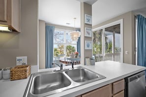 Eine Küche mit einem doppelten Waschbecken, ein Essbereich mit Tisch und Stühlen sowie ein Blick ins Freie durch große Fenster.