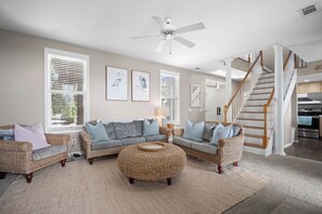 Ein Wohnzimmer mit Korbmöbeln, Deckenventilator und einer Treppe.