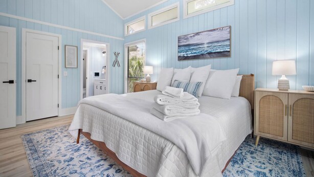 Een slaapkamer met een bed, nachtkastje, lamp, schilderij en een deur.
