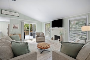 A living room with a sofa, a coffee table, a fireplace, a TV, and a sliding glass door leading to a deck. - Serene Island Getaway, Golf Cart Included, Pet Friendly - 101 Sea Otter (Fripp Island)