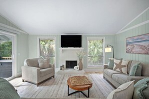 A living room with a fireplace, two sofas, a coffee table, and a TV mounted above the fireplace. - Serene Island Getaway, Golf Cart Included, Pet Friendly - 101 Sea Otter (Fripp Island)