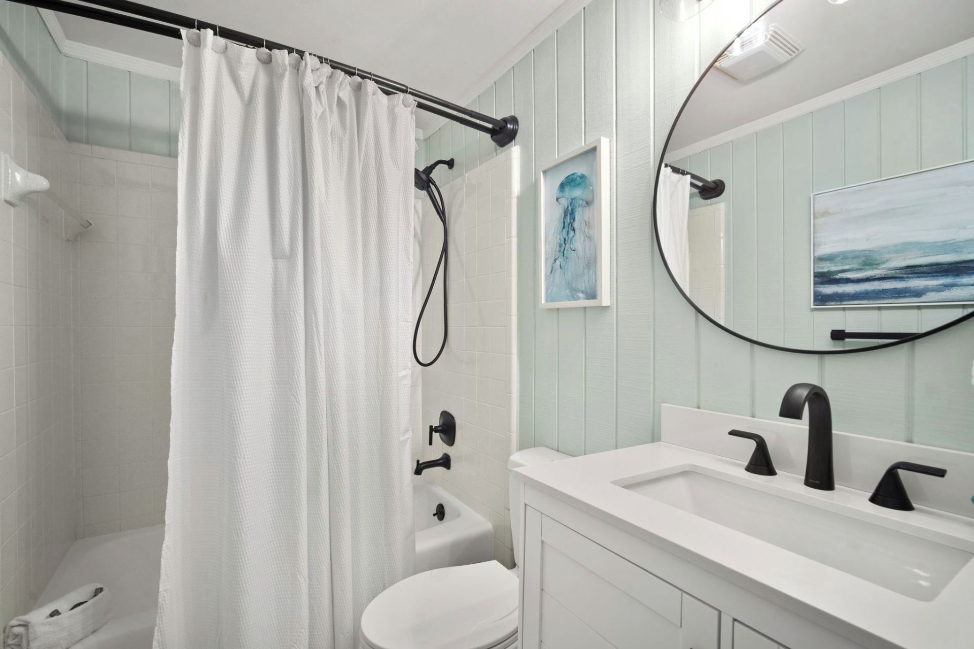 A bathroom with a shower, toilet, sink, and a round mirror with artwork.