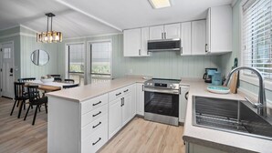 Een moderne keuken met witte kasten, een inbouwoven en een groot raam met jaloezieën.
