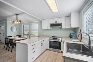 A modern kitchen with white cabinets, a built-in oven, and a large window with blinds. - Serene Island Getaway, Golf Cart Included, Pet Friendly - 101 Sea Otter (Fripp Island)