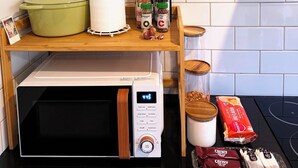 A kitchen counter with a microwave, a green pot, a roll of paper towels, spice bottles, garlic, a jar, and some packaged snacks. - Near Movie World & Wet'n'Wild | 2BR Home | Parking (Oxenford)
