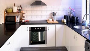 A modern kitchen with white cabinets, a stainless steel sink, a microwave, an oven, and a range hood. - Near Movie World & Wet'n'Wild | 2BR Home | Parking (Oxenford)