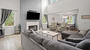 Een ruime woonkamer met een open haard, een televisie en een eethoek met een tafel en stoelen.