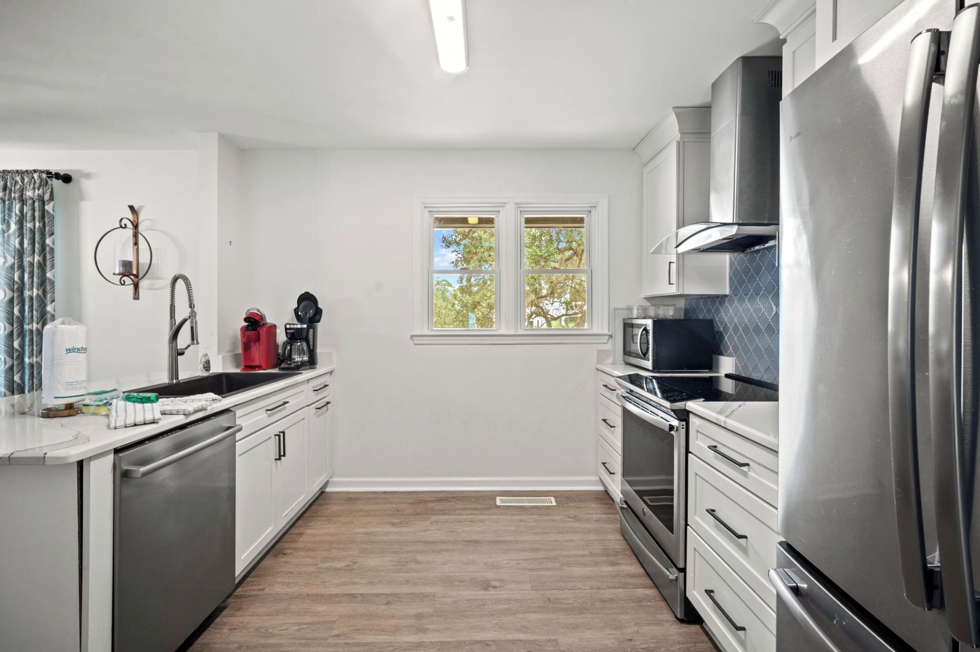 A modern kitchen with stainless steel appliances, a window with a view of trees, and a white interior.
