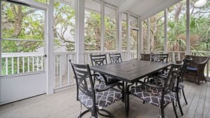 Een overdekt buitengebied met een tafel en stoelen, omgeven door witte hekwerk en grote ramen.
