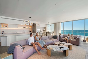 A modern living room with a large window, a kitchen area, and a seating area with a view of the ocean. - RISE | Luxury Penthouse with Pool (Coolangatta)
