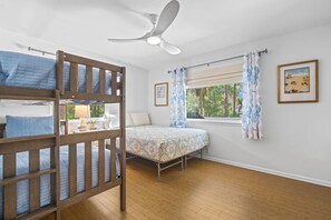 Ein Schlafzimmer mit Etagenbett, einem Einzelbett, einem Deckenventilator, einem Fenster mit Vorhängen und einem gerahmten Bild an der Wand.