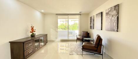 A spacious living area with a sliding glass door leading to a balcony, a dark wooden cabinet, and a brown leather chair.
