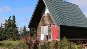 Una cabaña de madera con techo inclinado, una puerta roja y una ventana.