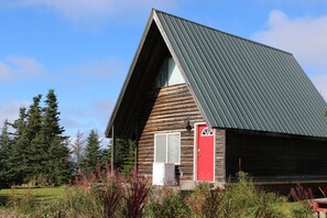 Eine Holzhütte mit geneigtem Dach, einer roten Tür und einem Fenster.