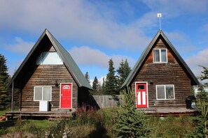 Dos cabañas de madera con puertas y ventanas rojas, una terraza de madera y un cielo despejado.