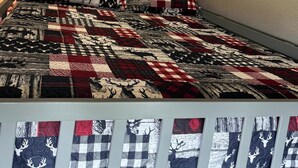 Una cama con colcha de diseño cervatillos, cabecero de madera y una lámpara.
