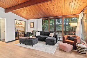 Un salon chaleureux avec un plafond en bois, un canapé d’angle, une petite table et une fenêtre avec des rideaux.
