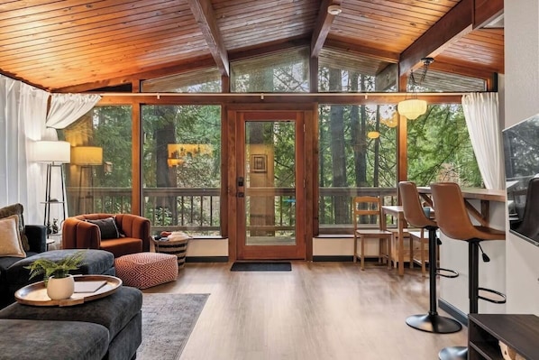 A spacious living area with a wooden ceiling, large windows, and a dining area with bar stools.