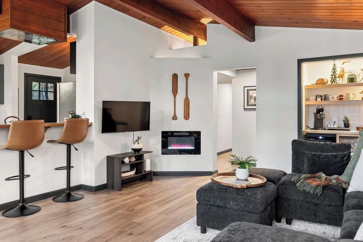 Un salon moderne avec une cheminée, un téléviseur et un coin bar équipé de tabourets.