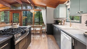 A modern kitchen with a gas stove, wooden chairs, and a view of the outdoors.