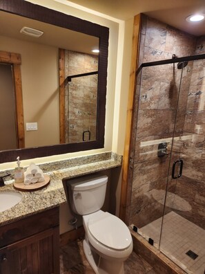 Ein Badezimmer mit einer Granit-Arbeitsplatte, einer weißen Toilette, einer Dusche mit Glastür und einem Holzwaschtisch.
