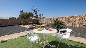 An outdoor patio with a stone wall, a windmill, and a round table with chairs. - Home2Book La Molina C, Rural Retreat (Antigua)