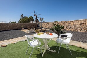 Een terras buiten, met een stenen muur, een windmolen en een ronde tafel met stoelen.