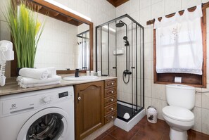 Een badkamer met een wasmachine, een douchecabine, een toilet en een wastafel met een spiegel erboven.