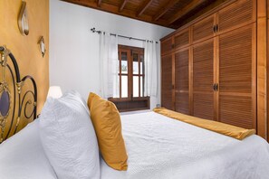Een slaapkamer met een bed, een houten kledingkast en een raam met gordijnen.