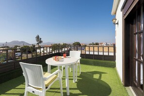 Un balcon avec une table et des chaises blanches, une vue sur le paysage urbain et un ciel dégagé.