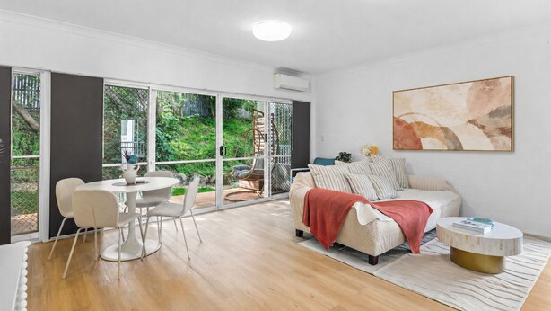 A modern living room with a sofa, a dining table with chairs, a large window, and a painting on the wall. - 2BR 2BA Indooroopilly | Walk to Shops & Bus (Indooroopilly)