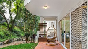 A patio with a swing chair, a wooden bench, and a glass door leading to a garden. - 2BR 2BA Indooroopilly | Walk to Shops & Bus (Indooroopilly)