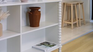 A white shelf with decorative items, a wooden stool, and a white wall with a phone and flowers. - 2BR 2BA Indooroopilly | Walk to Shops & Bus (Indooroopilly)