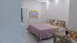 Una habitació petita i moderna amb un llit, una taula amb esmorzar i un quadre colorit a la paret.