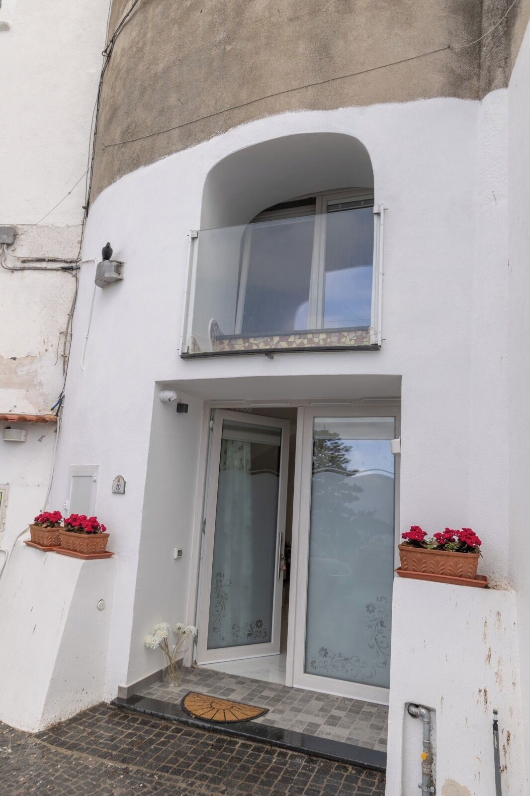 Ein zweistöckiges Gebäude mit Balkon, einer Tür mit Milchglas und Topfpflanzen.