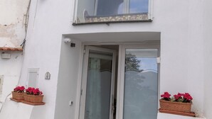 Un edifici de dues plantes amb un balcó, una porta amb vidre mat i plantes en testos.