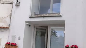Ein zweistöckiges Gebäude mit Balkon, einer Tür mit Milchglas und Topfpflanzen.