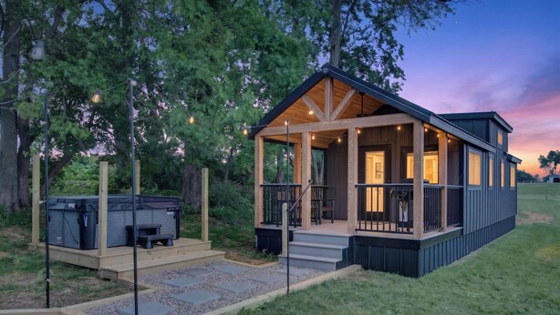 Eine moderne Hütte mit überdachter Veranda, Whirlpool und einer Terrassenfläche.