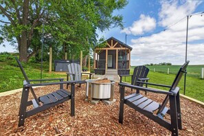 Ett utomhusområde med sittplatser, Adirondack-stolar, en eldstad och en träkonstruktion med en veranda.
