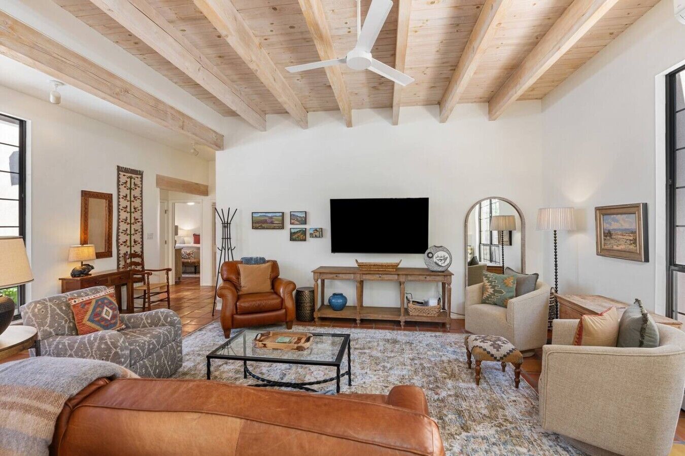 Un salon spacieux avec un plafond haut, un téléviseur à écran plat fixé au mur, et divers types de sièges, notamment un canapé en cuir, des fauteuils et un tapis à motifs.