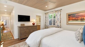 Un dormitorio con cama, cómoda, televisor y un cuadro.