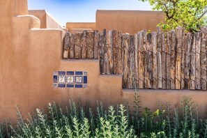 A building with a stucco exterior, a wooden fence, and a number plaque. - Two large patios with fountains and beautiful landscaping inside a private space. (Santa Fe)