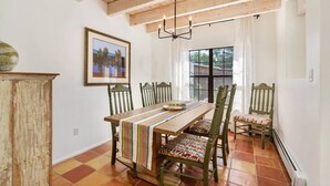 Un comedor con una mesa de madera, sillas, una araña y un ventanal con cortinas.