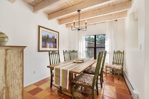 A dining area with a wooden table, chairs, a chandelier, and a window with curtains. - Two large patios with fountains and beautiful landscaping inside a private space. (Santa Fe)