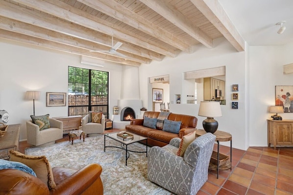 A spacious living room with a fireplace, wooden beams, and a large window. - Two large patios with fountains and beautiful landscaping inside a private space. (Santa Fe)