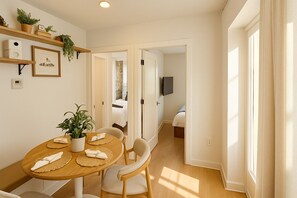 Un comedor con una mesa de madera, sillas, una planta en maceta y un televisor en la habitación contigua.