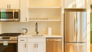 A modern kitchen with stainless steel appliances, white cabinetry, and a herringbone tile backsplash.